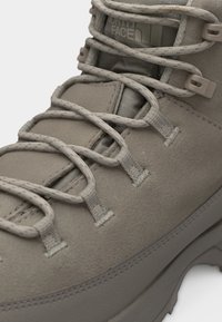 Κοντινό πλάνο καφέ μπεζ σουέντ μποτάκι πεζοπορίας με υφασμένα κορδόνια και μερικώς ορατό το λογότυπο The North Face στη γλώσσα.