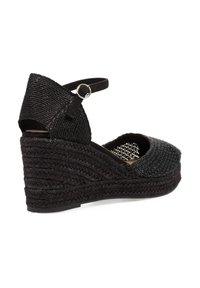 Sandalia de cuña negra trenzada con tira en el tobillo; parte superior de tela texturizada, puntera redonda y plantilla intermedia trenzada similar al yute. Detalle de hebilla en el tobillo.