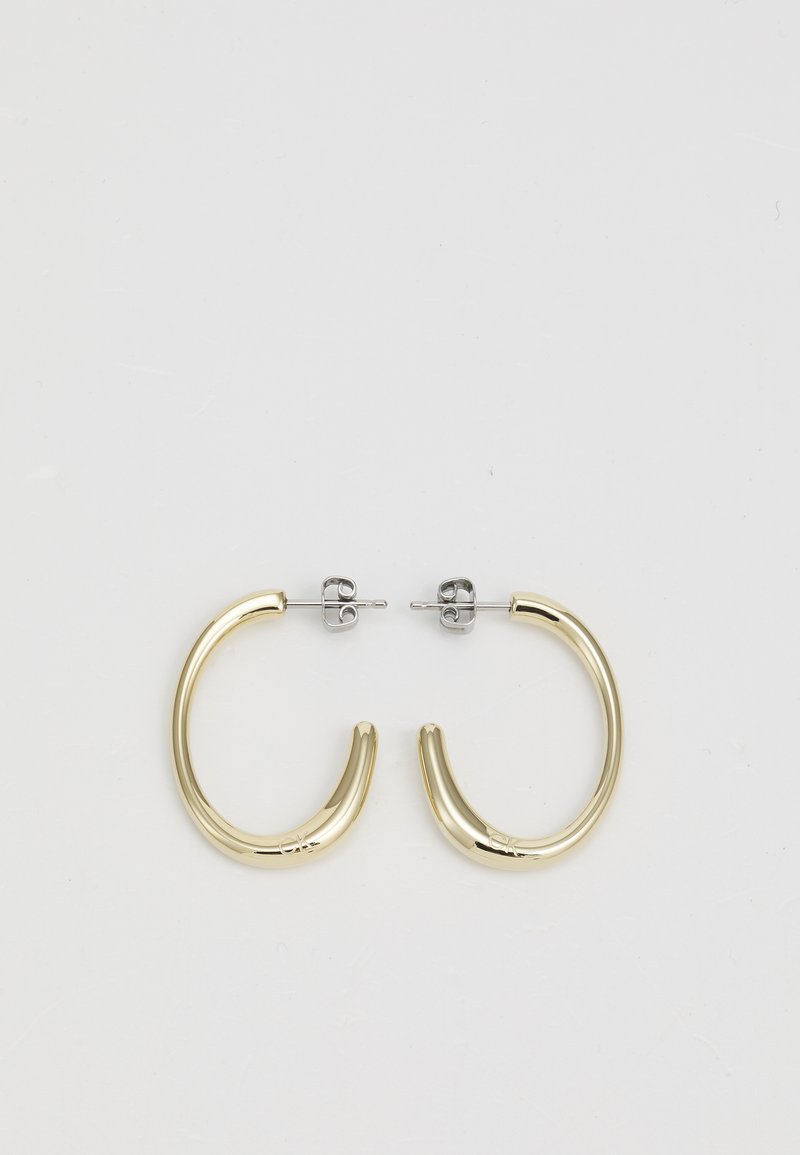 Orecchini a cerchio in tono oro con una superficie liscia e lucida. Presentano una forma curva e aperta e una chiusura in tono argento per un fissaggio sicuro.