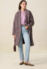 Manteau en chevrons texturé violet, chemise mauve claire, jeans bleu taille haute, ballerines marron imprimé serpent et un petit sac à main bordeaux.