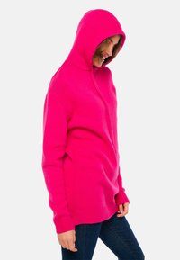 Sweat à capuche rose avec fermeture éclair sur le devant, poignets côtelés et texture lisse. Conçu avec une silhouette ajustée et une poche kangourou.