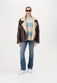 Brown leather jacket with a shearling collar, striped sweater in blue and beige, blue jeans, and white sneakers. Minimalist background.