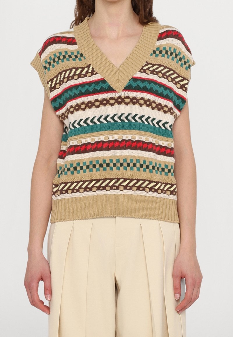 Chaleco de punto beige con cuello en V, con patrones multicolores de rayas y zigzags en rojo, verde y marrón. Mangas cortas, dobladillo acanalado.