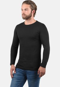 Sort langærmet t-shirt lavet af strækbart stof, med en rund halsudskæring og en tætsiddende pasform, parret med blå denim jeans.