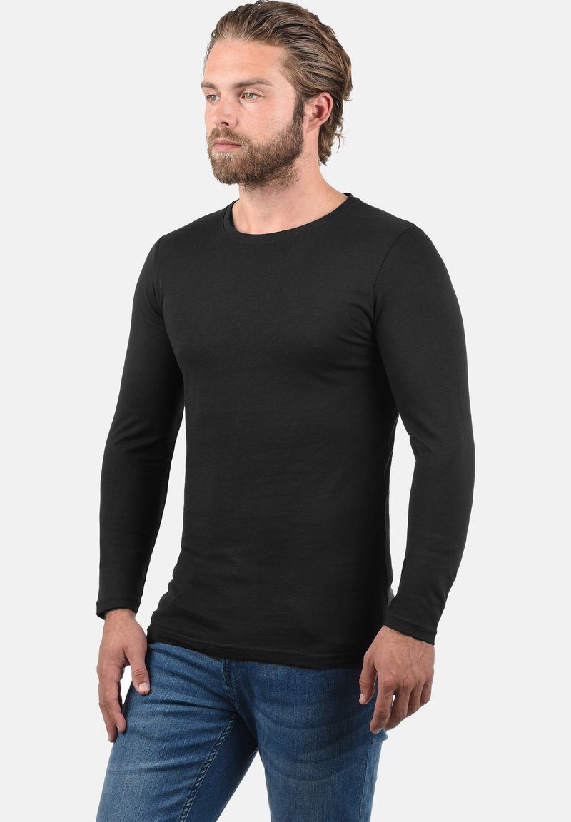 Sort langærmet t-shirt lavet af strækbart stof, med en rund halsudskæring og en tætsiddende pasform, parret med blå denim jeans.