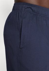 Pantalones cortos de algodón azul marino con cintura elástica y bolsillo lateral. La tela es suave, con una textura sutil y un corte holgado.