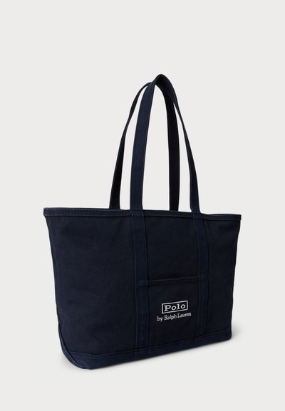 Jūras zila kanvas tote soma ar diviem gariem rokturiem, taisnstūra forma, ar priekšējo kabatu un izšūtu "Polo by Ralph Lauren" logo.