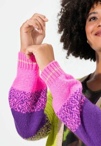Wielokolorowy sweter dzianinowy z różowymi, fioletowymi i zielonymi sekcjami. Posiada ściągacze przy rękawach oraz teksturowany wzór na rękawach.