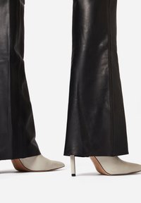 Zwarte leren broek gecombineerd met puntige, crème-kleurige hielen met een metalen stiletto-hak, die soepele texturen en een slank ontwerp benadrukken.