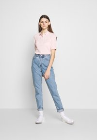 Polo shirt rosa chiaro con colletto e maniche corte, abbinato a jeans blu a vita alta e sneaker bianchi con suola decorata.