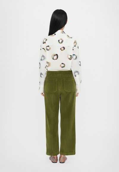 Camisa blanca con patrones circulares abstractos en varios colores, combinada con pantalones de pana verde de talle alto con bolsillos traseros.