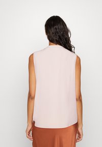 Haut sans manches, rose pâle, avec une texture lisse, un col rond et une coupe décontractée, vu de dos. Aucun système de fermeture ou motif visible.