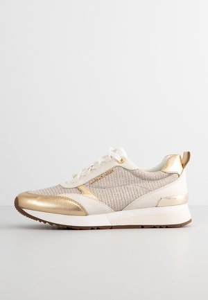 Beige og guld sneaker med tekstureret stof, læderdetaljer, hvid sål og brun slidbane, vist i sideprofil på en ensfarvet baggrund.