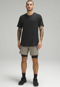 T-shirt noir à manches courtes avec un col rond, associé à un short beige. Caractérisé par des poches et un short de compression noir en dessous. Baskets noires.