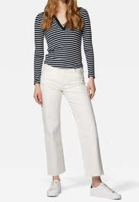 Pruhovaný dlouhý rukáv v námořnické modři a bílé, spárovaný s bílými džíny s vysokým pasem a širokými nohavicemi. Obuv zahrnuje bílé tenisky s černými detaily.