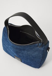 Denim shoulder bag with a black leather strap, top zipper closure, and a patterned blue exterior. Interior features a zip pocket.