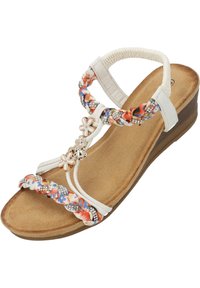 Sandale compensée blanche avec des brides tressées florales, des fleurs décoratives et des accents argentés. La semelle intérieure à texture de liège offre un confort supplémentaire.