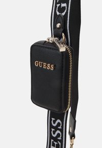 Sort faux læder taske med guld lynlås og "GUESS" logo. Har en aftagelig skulderrem med kontrastdesign i hvid og sort.