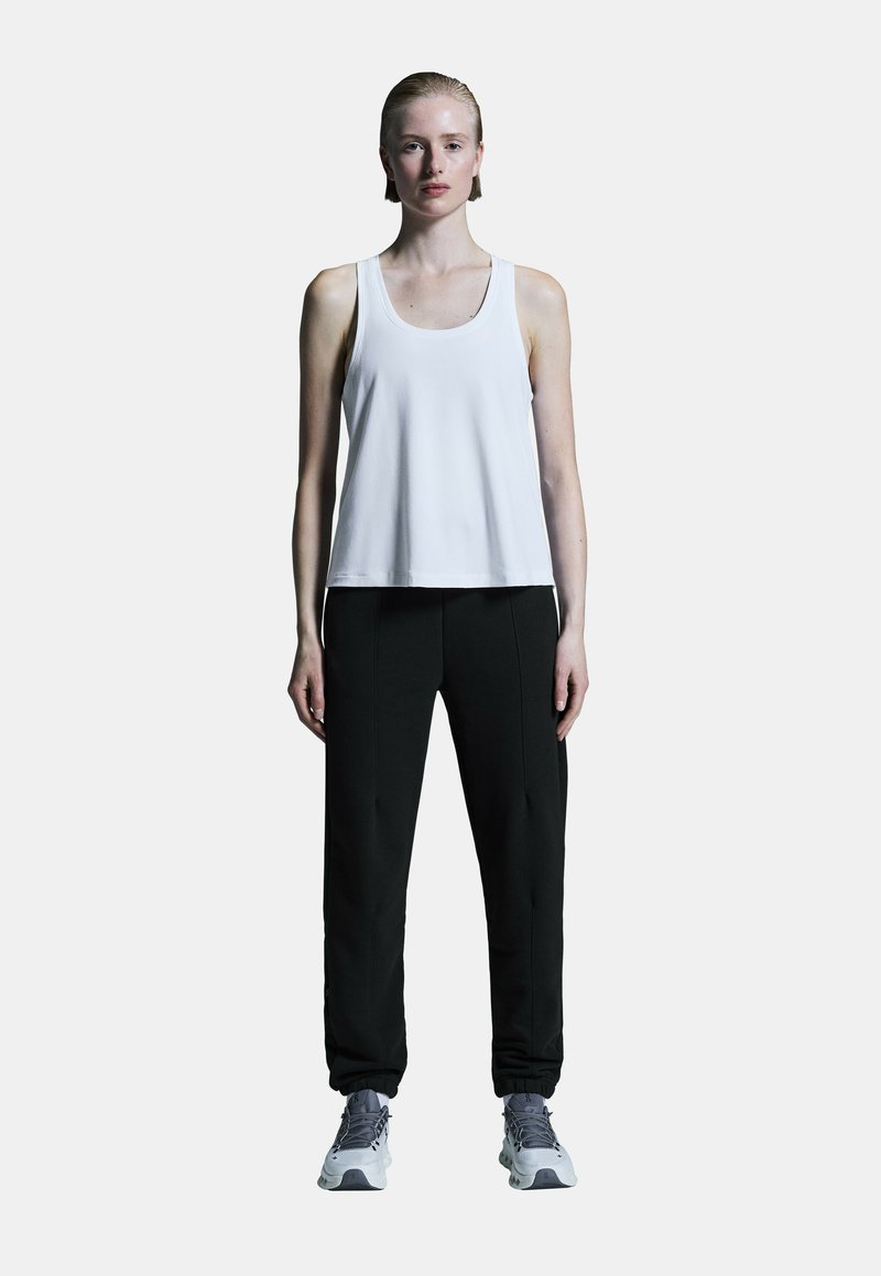 Top sans manches blanc avec un col rond, associé à un pantalon de jogging noir fuselé et des chaussures de sport grises. Design et coupe minimalistes.
