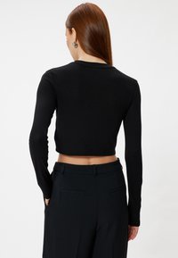 Zwarte cropped top met lange mouwen, gemaakt van soepel materiaal, met een ronde hals. Draagt bij een op maat gemaakte zwarte broek met zijzakken.