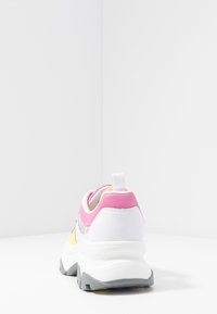 Bílé tenisky s růžovými a žlutými akcenty, texturovanými síťovanými částmi, silnou podrážkou a poutkem vzadu. Zaoblený tvar s moderním designem.