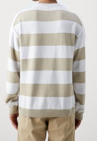 Pull rayé en blanc et beige clair. Texture en tricot, poignets et ourlet côtelés, col rond, coupe loose avec épaules tombantes.