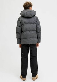 Giacca imbottita grigia con ampio cappuccio, caratterizzata da sezioni trapuntate. Abbinata a pantaloni cargo neri e scarpe color camoscio. Texture morbida e liscia nel complesso.