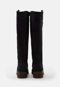 Botas largas de ante negro con cremallera en la parte trasera, con tacón de madera y textura suave, que exhiben un diseño y silueta minimalistas.