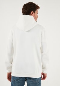 Valkoinen huppari, valmistettu pehmeästä puuvillasekoitteesta, jossa on iso huppu, resorit hihansuissa ja helmassa, sileä pinta ja minimalistinen design.