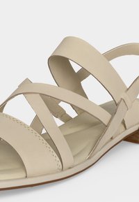 Sandale plate beige avec plusieurs brides croisées et un petit talon en bois, conçue pour un usage décontracté.