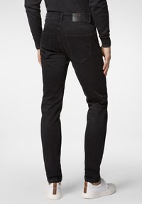 Svarta denimjeans med smal passform, utrustade med bakfickor, en läderpatch i midjan och vita sneakers med bruna detaljer.