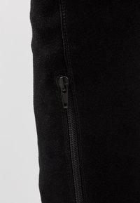 Tissu en daim noir à texture lisse, doté d'une fermeture éclair latérale en métal noir, mettant en valeur un design élégant et ajusté.