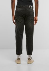 Pantalones de mezclilla negros con un ajuste relajado, que cuentan con dos bolsillos traseros y una etiqueta de la marca en la cinturilla. La textura es suave con un ligero brillo.