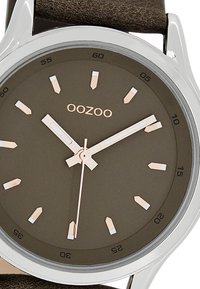 Round watch with a dark brown matte dial, silver-tone case, rose gold markers, and brown leather strap. Clean design with minimal accents.