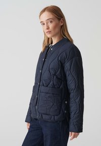 Giacca trapuntata blu navy con colletto rotondo, bottoni a scatto e tasche laterali; presenta un design testurizzato e imbottito e una forma leggermente aderente.