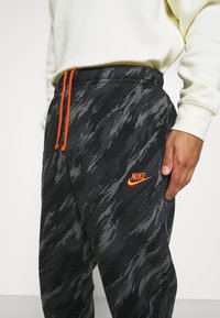 Svart- och gråmönstrade träningsbyxor med ett orange Nike-logga, utrustade med elastisk midja med orange dragsnören och ett texturerat tyg.