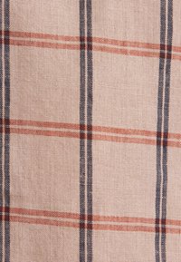 Tissu beige à texture tissée présentant un motif à carreaux composé de rayures verticales bleu foncé et de rayures horizontales rouge orangé.
