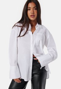 Witte oversized button-up shirt met lange mouwen en een zak; gemaakt van lichtgewicht stof; gedragen met zwarte leren broek.