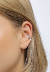 Silver örhänge med en vriden design, bärs på den övre delen av örat. Slät textur, samtida form och lyfter fram örats naturliga kontur.