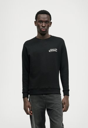 Juodas džemperis apvalia iškirpte, su reljefinėmis rankovėmis ir apatine dalimi. Krūtinėje yra baltas logotipo mundūras. Minkšta, tekstūruota medžiaga, laisvas kirpimas.