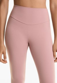 Hoge taille, aansluitende legging van zacht roze stof. Glad textuur met een brede tailleband en minimale naaddetails voor een gestroomlijnde uitstraling.