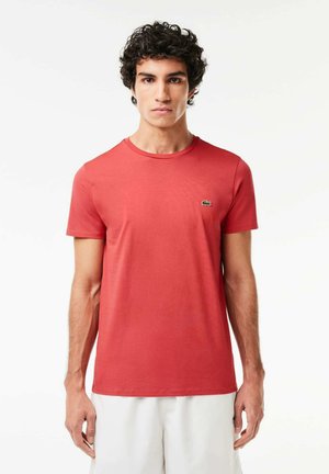 T-shirt rossa a maniche corte in cotone. Presenta un colletto rotondo e un piccolo logo verde sul petto. Texture liscia.