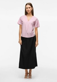 Ljusrosa T-shirt med V-ringning och korta ärmar, som matchas med en svart lång kjol. Outfiten består av enkla former och enfärger, vilket skapar en kontrast.