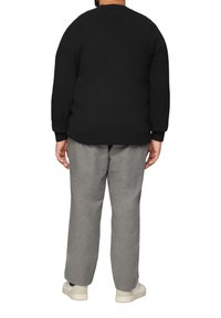 Schwarzer Sweatshirt mit rundem Hals, kombiniert mit hellgrauen Hosen und weißen Sneakers, von hinten betrachtet. Schlicht, lockere Passform.