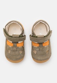 Scarpe per bambini di colore marrone e arancione, realizzate in suede, con sezioni ritagliate, una chiusura in Velcro e una suola in gomma. Taglia 18 indicata all'interno.