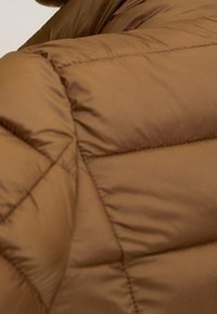 Hnědá péřová bunda s diamantovým prošíváním, hladkým povrchem a vysokým límcem. Materiál vypadá měkký a syntetický.