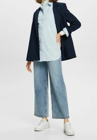 Mörkblå kavaj, ljusblå skjorta med knappar och vida ljusdenimjeans. Vita sneakers fulländar outfiten.