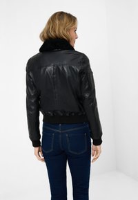 Black leather bomber jacket with a faux fur collar, ribbed cuffs, and hem, featuring a side pocket and a smooth texture.
