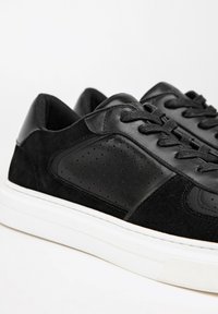 Černé tenisky s kombinací hladké kůže a semiše, s perforovanými detaily, bílou gumovou podrážkou a plochými černými tkaničkami.