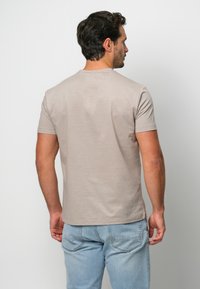 Ljusbeige kortärmad t-shirt med rund halsringning, tillverkad av ett mjukt tyg, i kombination med ljusblå jeans, som visar en avslappnad passform.